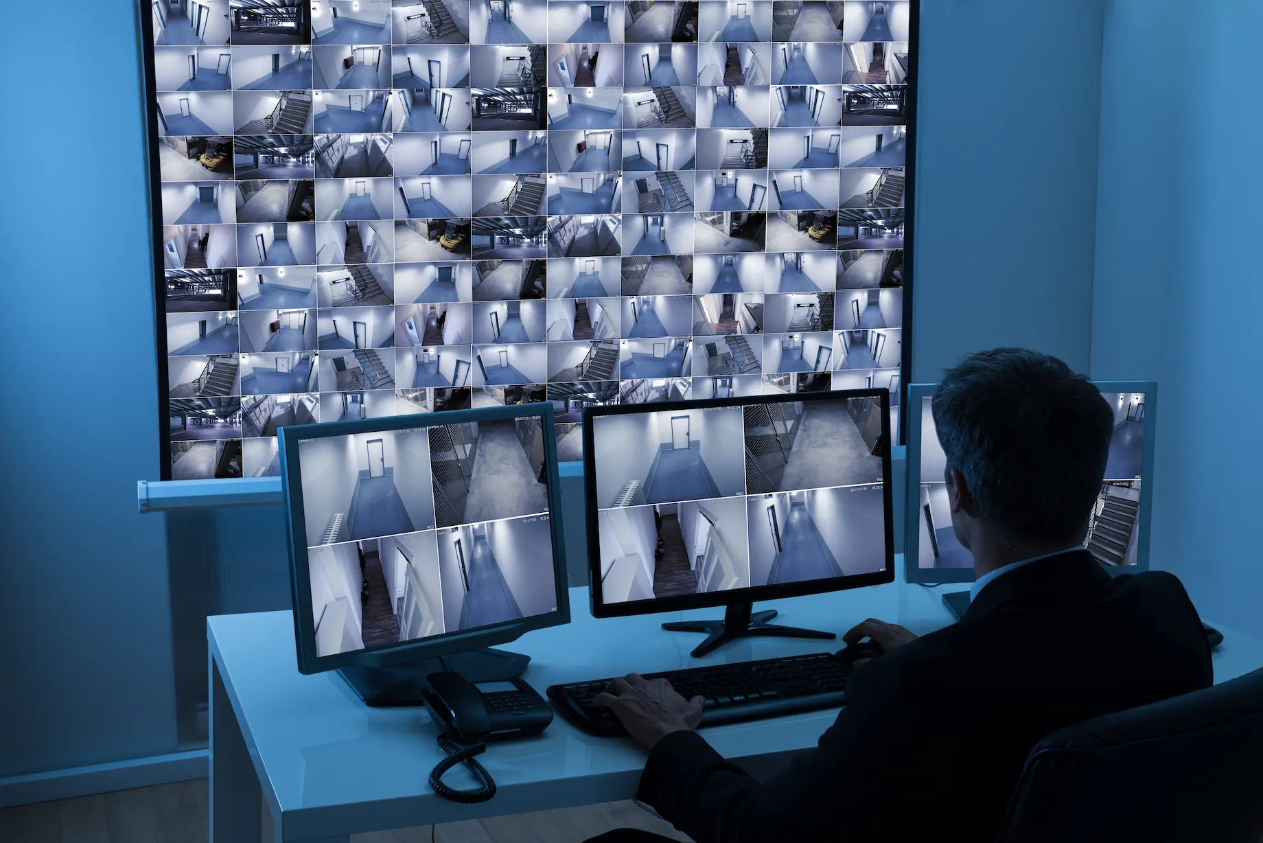 Security operator monitoring multiple CCTV camera feeds in a surveillance control room.