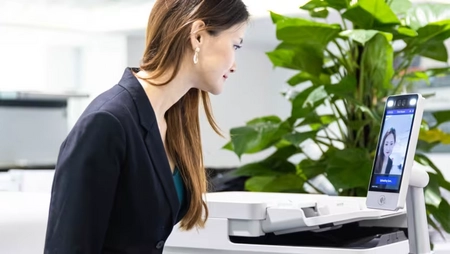 A woman uses facial recognition technology for secure printing in an office.
